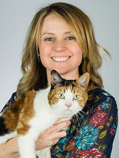 A woman with blonde hair holding a calico cat smiles towards the camera