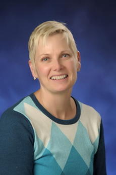A woman with short blonde hair and blue and white sweater smiles towards the camera