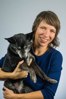 A woman holding a small dog smiles towards the camera